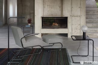 Loungehoek met zwart-wit gestoffeerde fauteuil, voetenbankje en bijzettafel in minimalistische betonruimte met open haard.