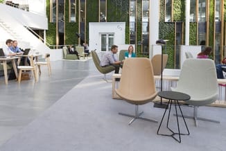 Modern kantoor met beige en groene designstoelen, houten werkplekken, groene wandbeplanting en medewerkers in verschillende z