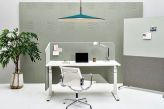 Kantoor werkplek met wit verstelbaar bureau, witte bureaustoel, groene akoestische wandpanelen, blauwe hanglamp en plant.