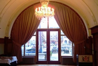 Elegante ontvangstruimte met rode gordijnen, kristallen kroonluchter, grote ramen met uitzicht op water en klassieke houten d