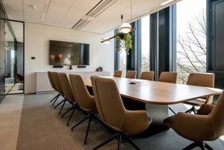 Moderne vergaderruimte met wit blad tafel, bruine draaistoelen, wandmontage TV, hangende groene planten en grote ramen met ui