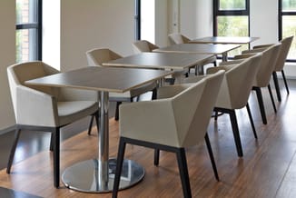 Moderne vergaderruimte met drie rechthoekige tafels, beige stoelen met zwarte poten, houten vloer, grote ramen en natuurlijk