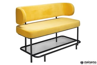 Gele bank met cylindrische rugkussen, zwart metalen frame en lage open opbergplank onderaan.