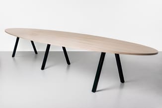 Lange ovale vergadertafel met licht houten blad en zwarte schuine poten, frontaal weergegeven.
