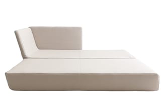 Beige loungebank met lage zitting, hoge rugleuning en zijkussen tegen witte achtergrond.