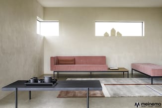 Minimalistische inrichting met roze corduroy sofa, zwarte tafels, grijze stoffen pouf en hogevensterraam met woondecoraties.