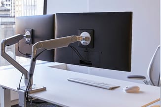 Moderne werkplek met twee zwarte monitoren op verstelbare monitorarmen, wit bureau met toetsenbord en muis, uitzicht op kanto