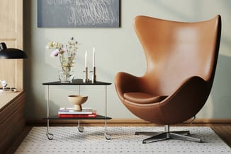 Bruinleren eivormige fauteuil met zwart onderstel naast zwarte salontafel op wieltjes met boeken en bloemen in glazen vaas.