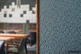 Blauwe akoestische wandbekleding met textuurpatroon, in kantooromgeving met houten meubels en witte bovenliggende structuur.