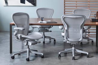 Moderne kantoorstoelen met grijs mesh-ruggesteun en wit zitgedeelte rond houten vergadertafel in lichte kantoorruimte.