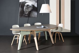 Ovale vergadertafel met naturel houten blad en mint groene poten, omgeven door witte stoelen met houten poten. Hanglamp en mu
