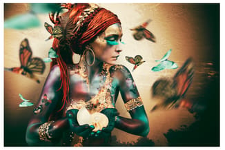 Vrouw met rood haar, turquoise gezichtsbody art en gouden accenten, omringd door vlinders in kunstzinnige compositie.