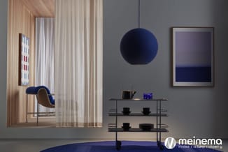 Moderne kantoorruimte met grijze wand, donkerblauwe hanglamp, metalen wandplank met servies, blauwe bureaustoel bij houten ra