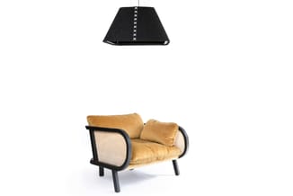 Gouden loungestoel met zwart houten frame en rotan zijpanelen, met bijbehorende zwarte hanglamp met witte stiksel.