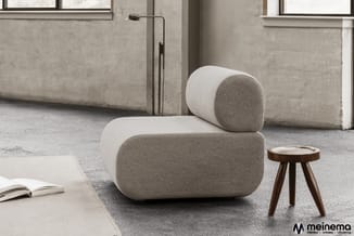 Grijze modulaire bank met ronde vormen in betonnen ruimte, houten bijzettafel en leeslamp; boek op witte tafel links.