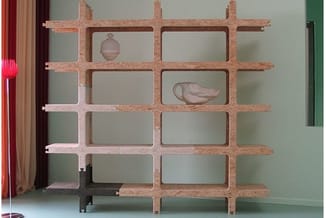Houten open kasten met kruispatroon tegen groene muurwand. Enkele items geplaatst in compartimenten.