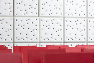 Witte akoestische tegels met grijze stippen en rode geluidsabsorptie panelen in onderaanzicht.