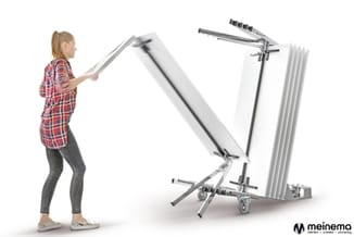 Vrouw in rood geruite blouse demonstreert het opvouwen van een mobiel whiteboard-systeem met metalen frame en wielen.