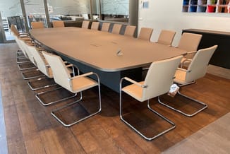 Moderne vergadertafel met beige blad en donkere onderkant, omringd door beige en witte kantoorstoel met chromen poten in verg