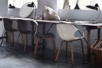 Werkplek met lange zwarte tafel, zwarte en witte stoelen met houten poten, zwarte bureaulampen en witte accessoires op grijze