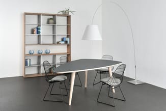 Vergaderruimte met grijze tafel, houten poten, vier zwarte draadstoel, houtkleurige kasten, boogvloerlamp en witte wandspiege