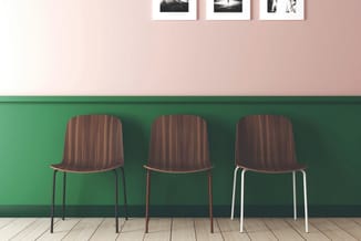 Drie houten stoelen met geribd zitgedeelte tegen groene muurdecoratie in kantooromgeving.