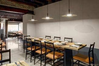 Moderne eetkamer met lange houten tafel, zwarte stoelen met okergele zitting, drie hangende UFO-vormige pendellampen, betonne