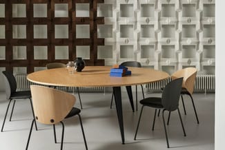 Ronde houten vergadertafel met zwarte poten, omgeven door houten en grijze stoelen met zwarte zitting in moderne kantoorruimt