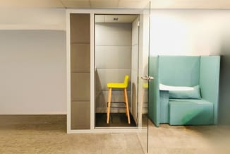 Minimalistische kantoorruimte met gesloten belcel met gele barstoel, groene modulaire zitbank en witte wanden.