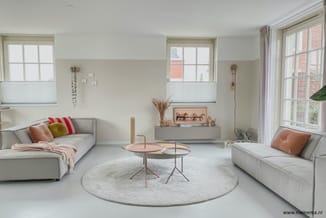 Moderne woonkamer met twee grijze banken, rond wit vloerkleed, twee ronde tafels in roze/wit, wandmeubel met framed artwork,