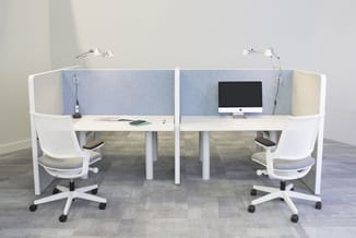 Twee witte werkplekken met blauwe akoestische schermen, witte bureaus, witte ergonomische stoelen en bureaulampen in een kant