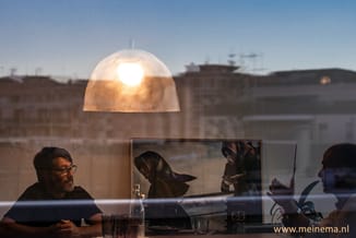 Vergaderruimte met goudkleurige hanglamp boven tafel, deelnemers aan vergadering met uitzicht op stadsgebouwen.