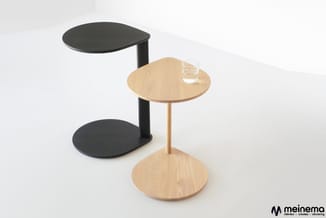 Twee moderne bijzettafels met ronde bladen: één in natuurlijk hout met houten voet, één in zwart met zwarte voet. Op de houte