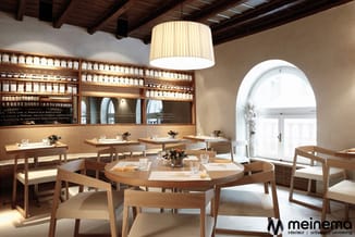 Modern restaurant interieur met ronde houten eettafels, houten stoelen met crème kussens, wandkasten met potten, hanglamp en