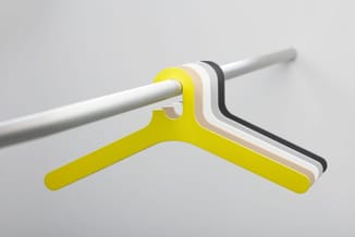Kledinghanger in geel, wit, beige en zwart, opgehangen aan een grijs buisprofiel tegen neutrale achtergrond.