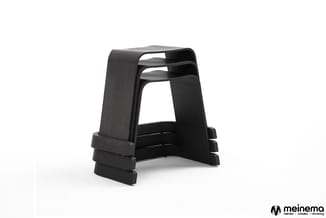 Zwarte stapelbare kunststof krukken gestapeld, modern ontwerp met ergonomische zitting en voetsteun.