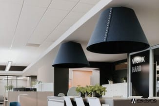 Moderne kantoorruimte met twee grote zwarte hanglampenkappen, witte plafondpanelen, beige werkplekken met groene plant en "WO