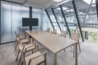 Moderne vergaderruimte met lichte houten tafel, beige stoelen, zwart wandscherm, en glazen wanden met stalen constructie.