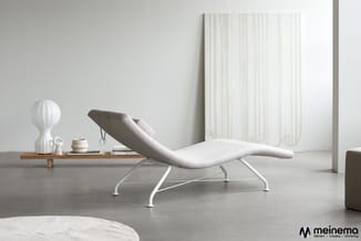Witte loungestoel met grijze metalen onderstel in minimalistisch interieur met houten plateau, decoratieve objecten en groot