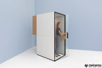 Witte belcel met zwart frame en houten zijpaneel. Vrouw staat binnen in de gesloten cel met gele tas. Meinema-logo rechtsonde