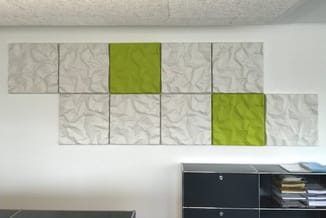 Wandpanelen in beige en groen, rechthoekig gerangschikt boven zwart kantoormeubel tegen witte muur.