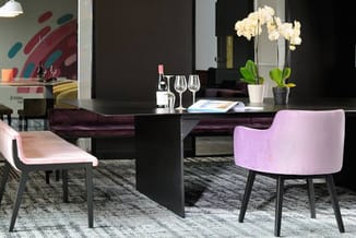 Moderne vergaderruimte met zwarte vergadertafel, roze en beige stoelen, witte orchideëen, glazen en wijnfles op tafel.