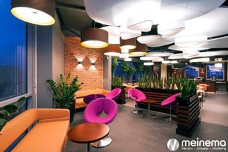 Modern kantoorinterieur met oranje en roze ronde zitmeubels, houten plantenbakken, hangende design lampen en bakstenen muur.