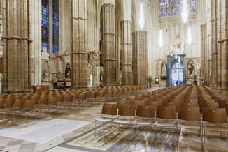 Bruine stapelstoelen met metalen frame in rijen opgesteld in een gotische kathedraal met hoge pilaren en glas-in-loodramen.