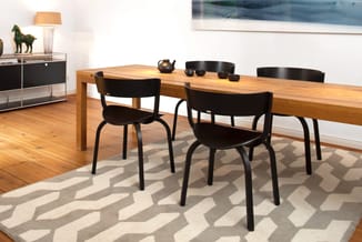 Houten eettafel met zwarte stoelen in minimalistische eetkamer met geometrisch tapijt en zwart dressoir.