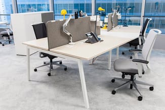Modern kantoor met witte bureau's, grijze akoestische schermen, zwarte en grijze bureautoelen, en grote ramen met uitzicht.
