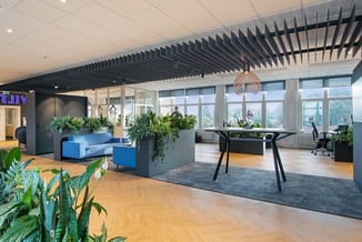 Modern kantoorinterieur met blauwe bank, zwarte werkstafel, houten vloer, zwarte slatwall, hangende lamp en groenvoorziening.
