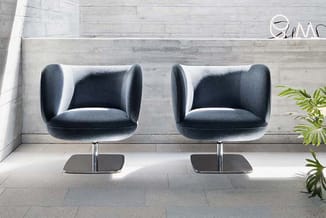 Twee donkergrijze fauteuils met chromen voet tegen betonnen wand in minimalistisch interieur, naast plant.