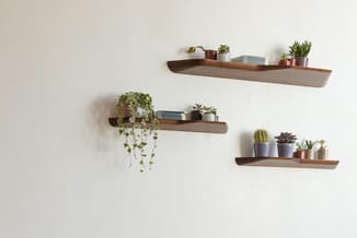 Vier houten wandplanken in natuurtint met verschillende decoratieve artikelen, planten en boeken tegen een witte muur.
