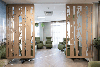 Decoratieve houten scheidingswanden met boompatroon in moderne kantoorruimte met groene fauteuils en hangende planten.
